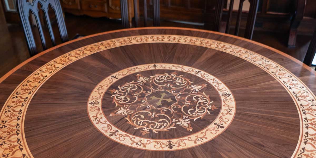 Luxury custom wood inlay tabletop featuring a large central floral medallion and an intricate scrollwork border. Bespoke handcrafted furniture design by Czar Floors.